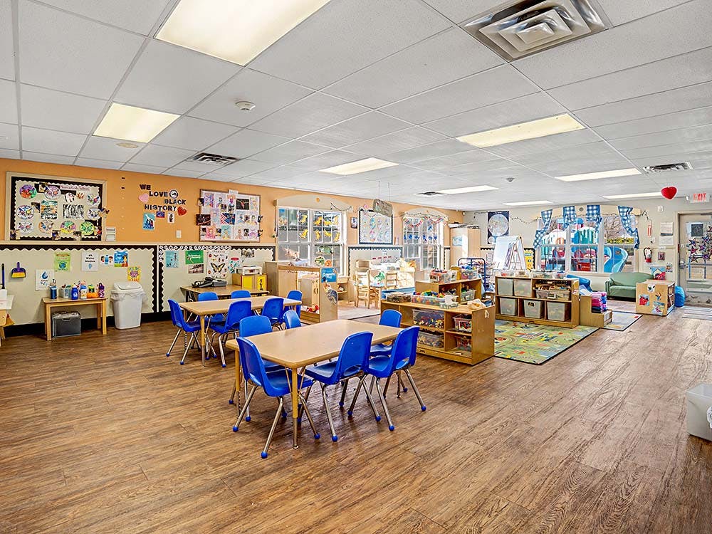 Empty classroom with small tables and chairs, bulletin boards, and learning areas