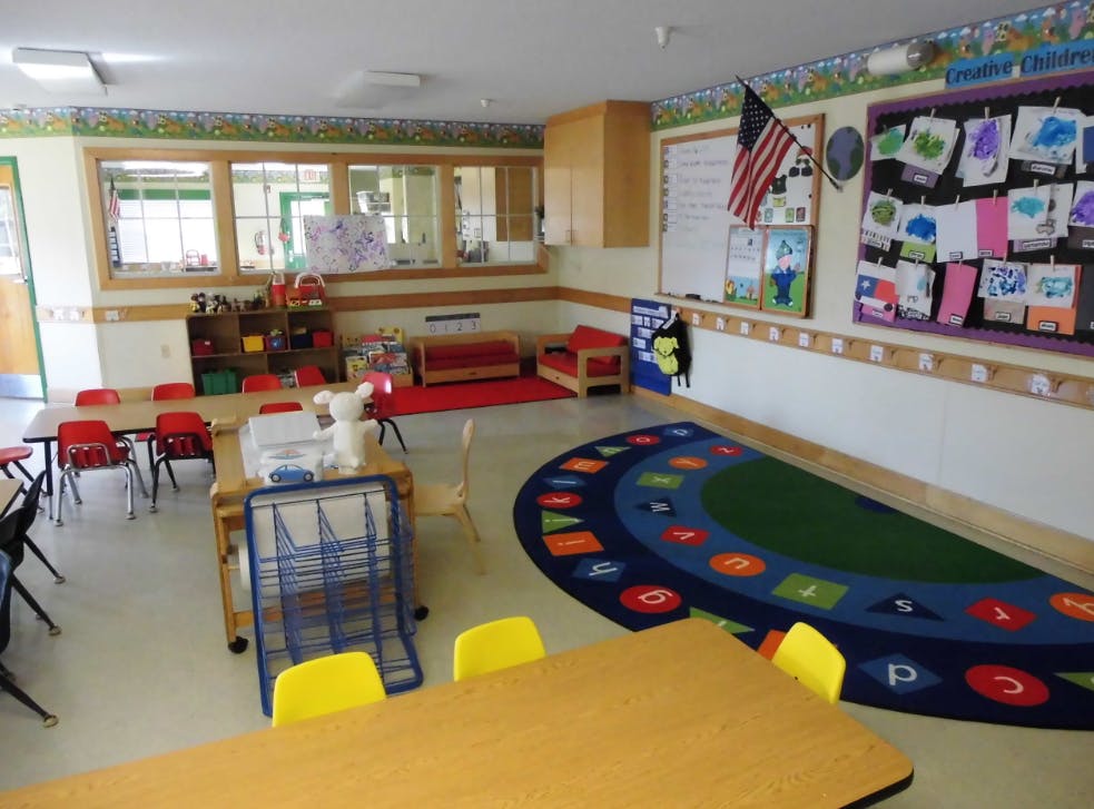Classroom with small tables and chairs, a colorful rug, and artwork on the wall