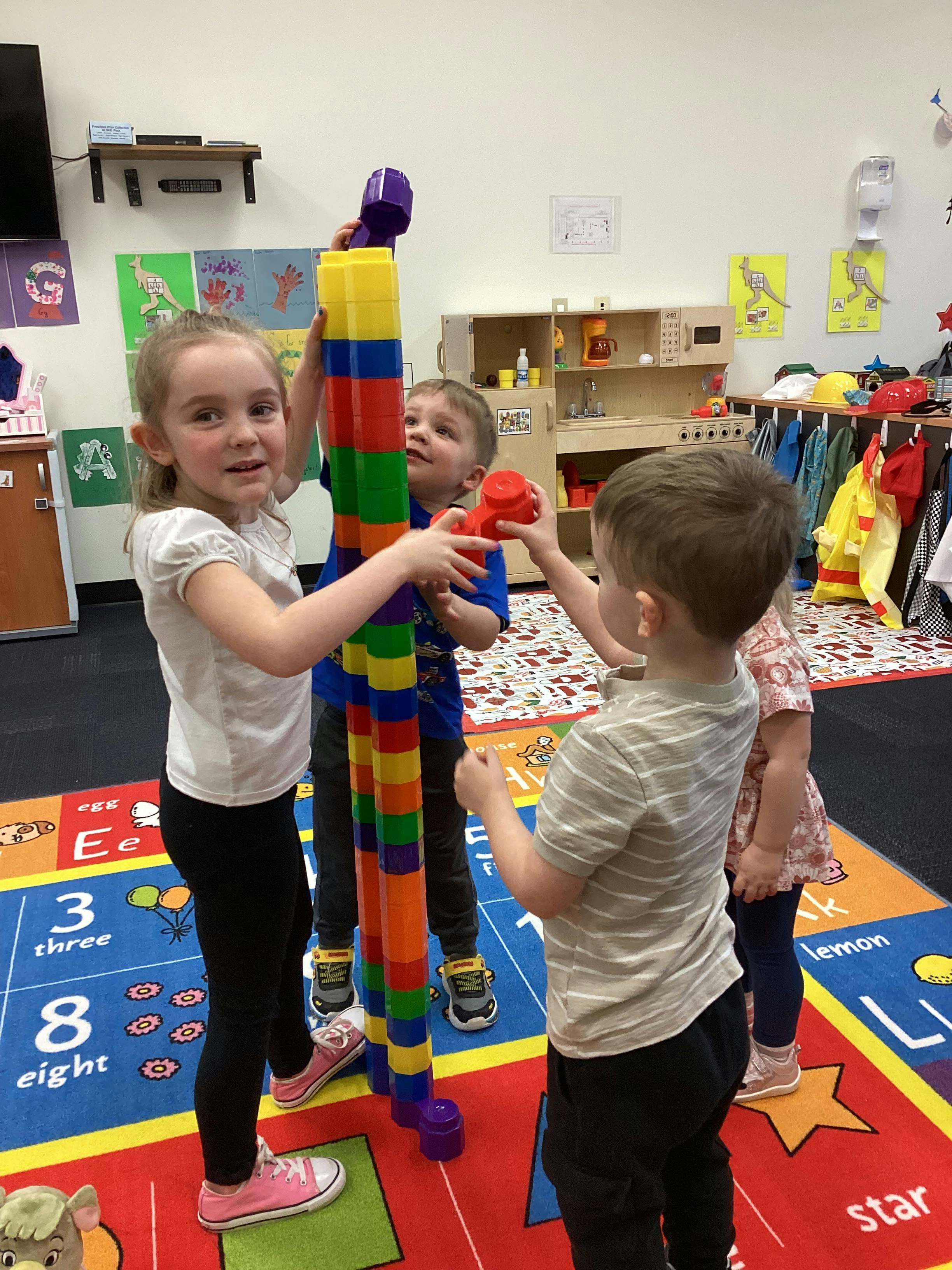 Three children playing with colorful building blocks in a classroom