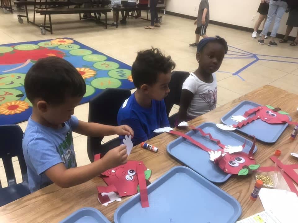 Three children at a table doing crafts with crafts with red paper crafts