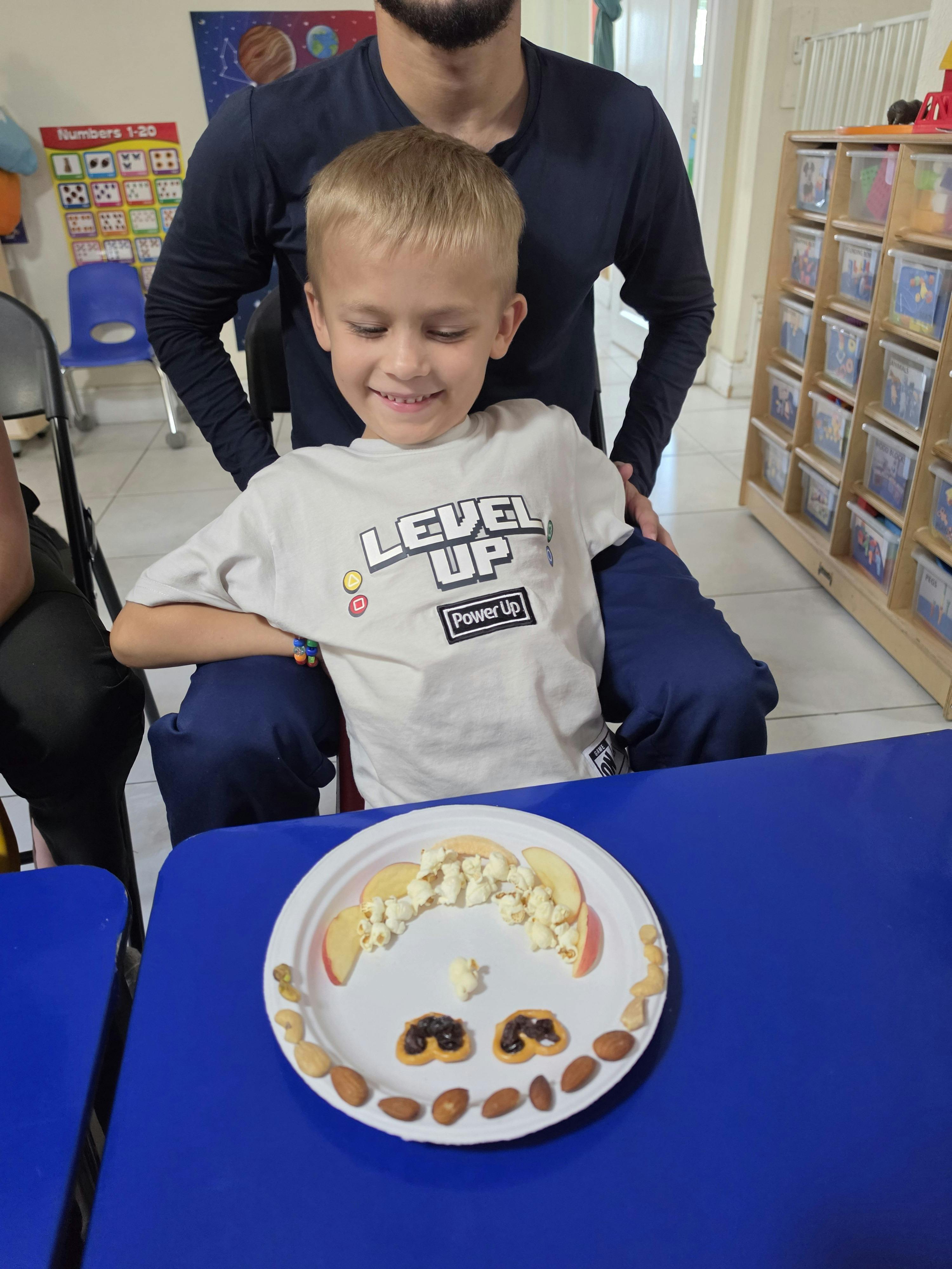 A child sitting in front of a plate decorated with snacks in a classroom
