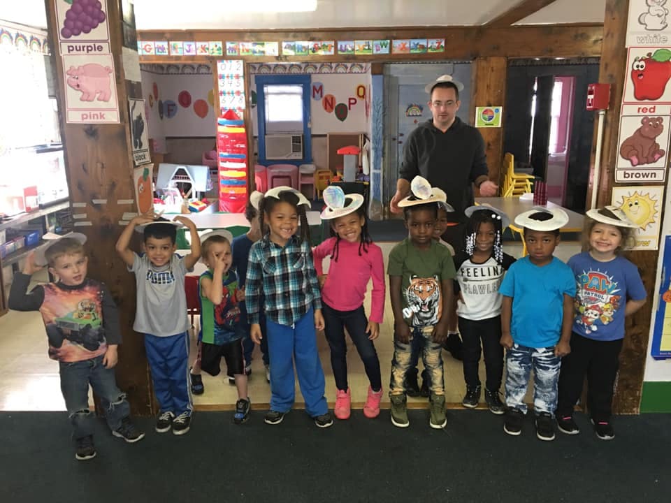 Adult and children in a classroom, some children wearing hats