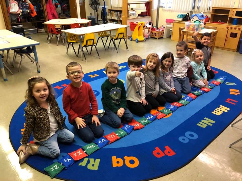 Children sitting on a blue alphabet rug in a classroom