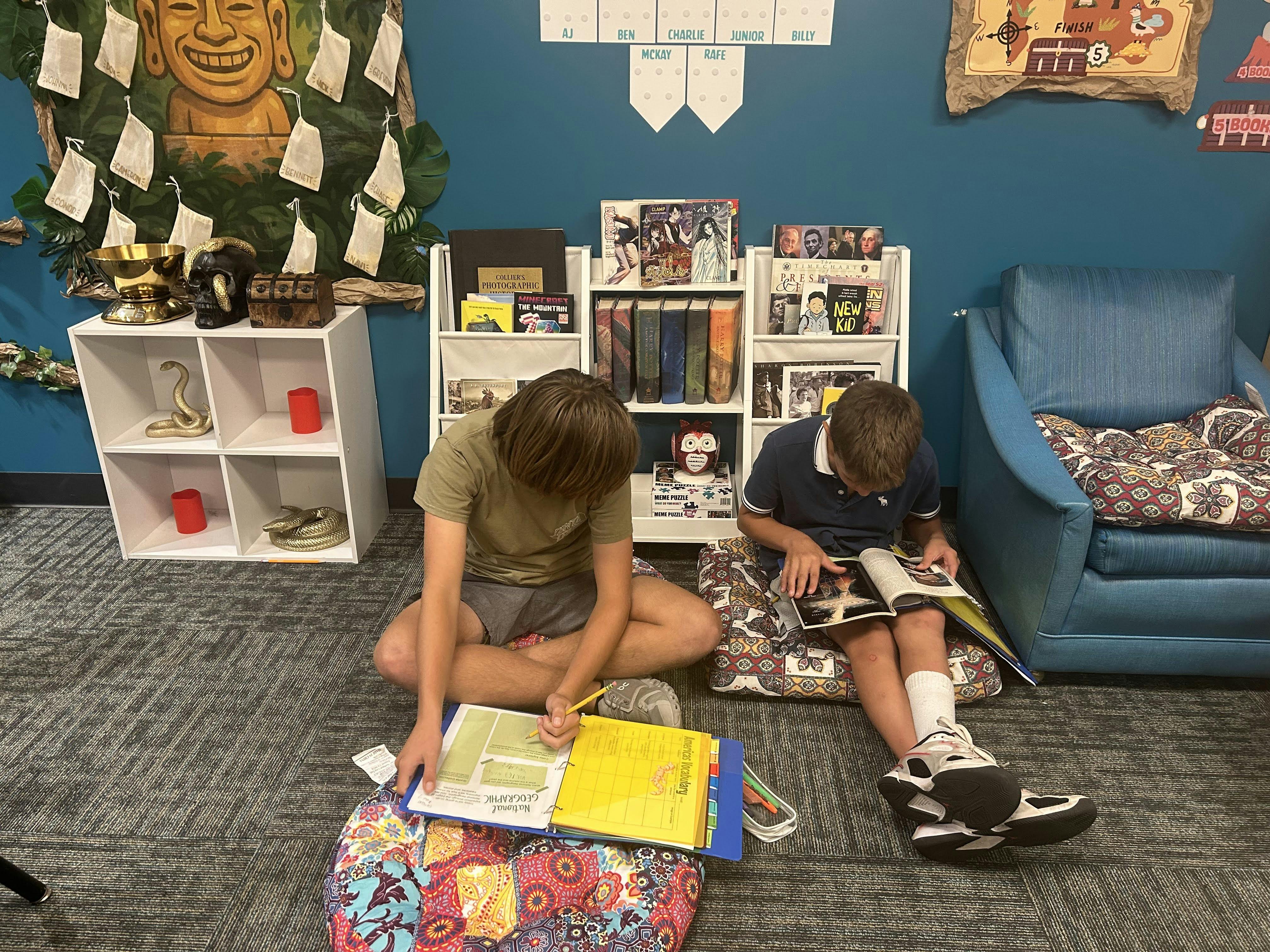 Two teens sitting on the floor reading and studying in a classroom