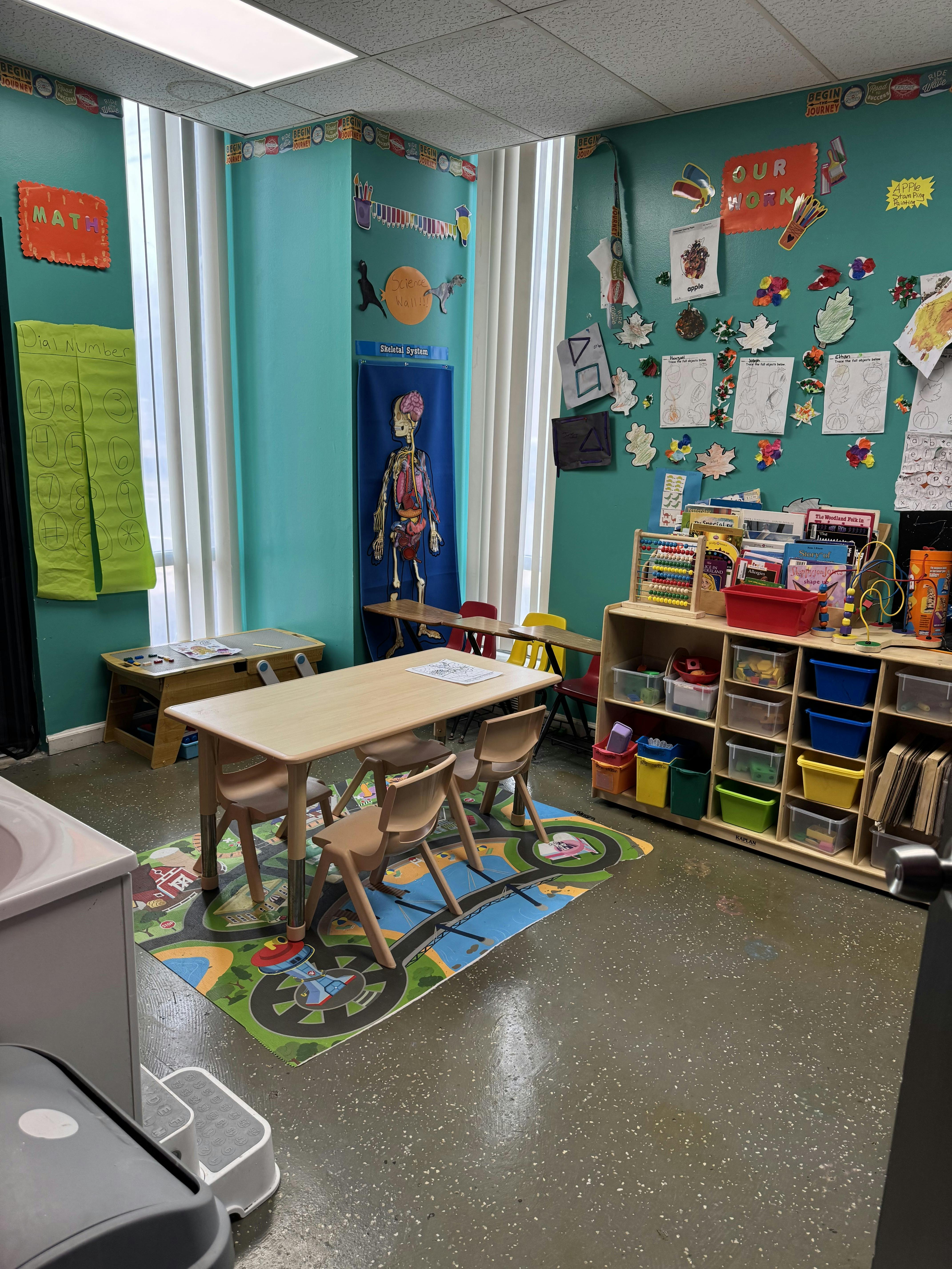 Classroom with small tables and chairs, toys, and educational posters on the walls