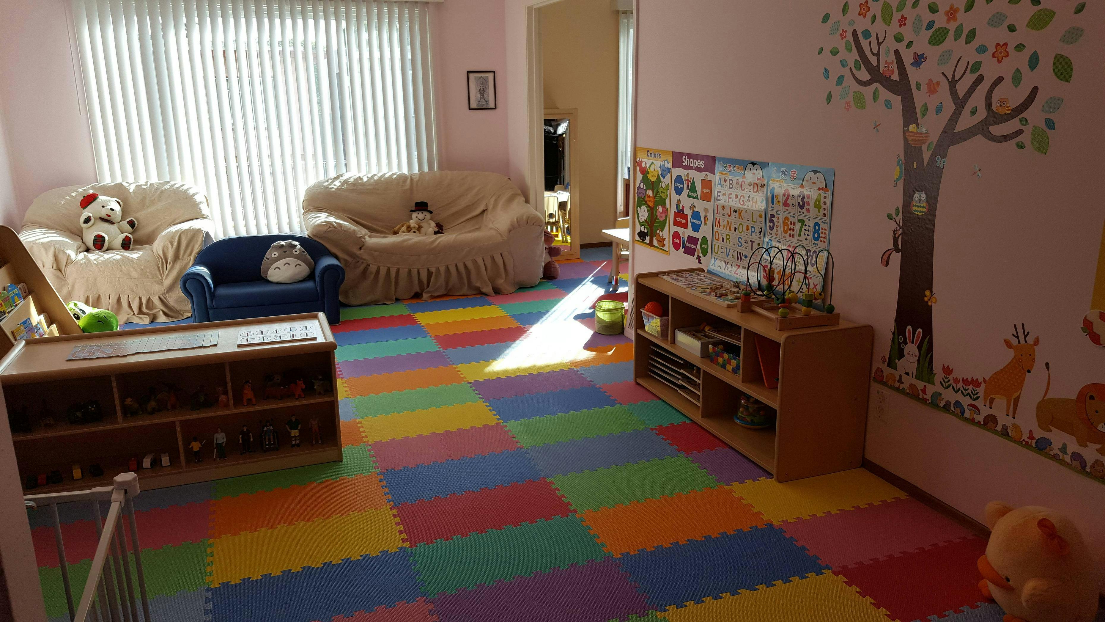 Playroom with colorful floor mats, sofas, and a wall mural
