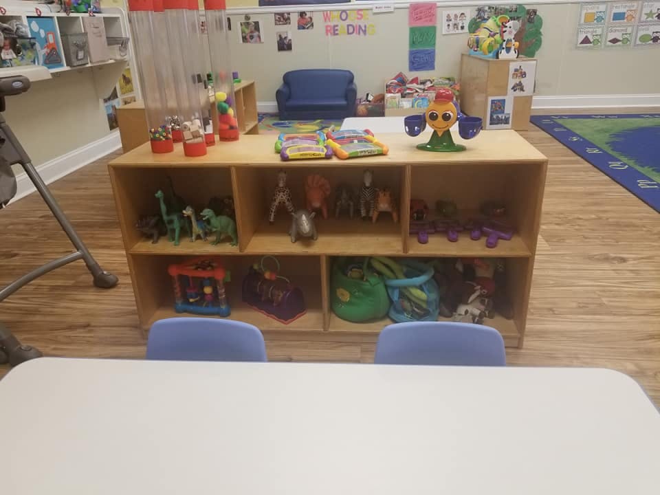 Classroom with wooden toy shelf, blue chairs, and white table