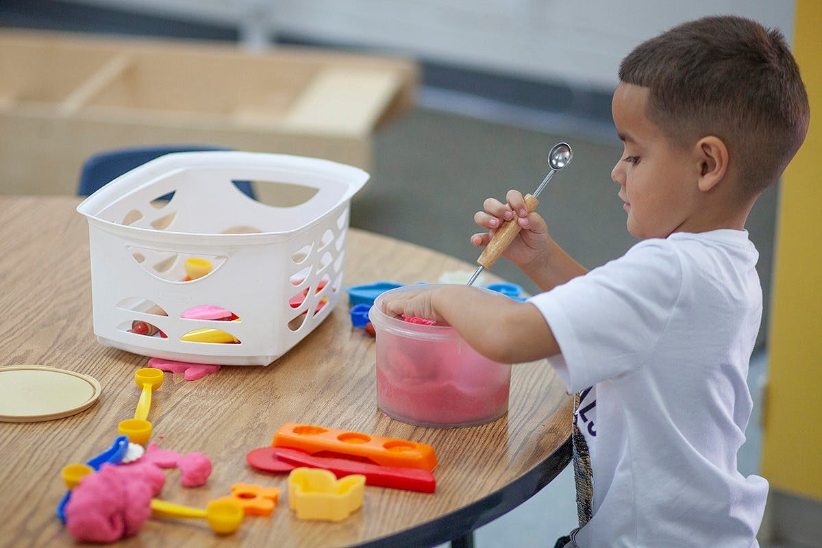 Child playing with modeling clay and tools at a table