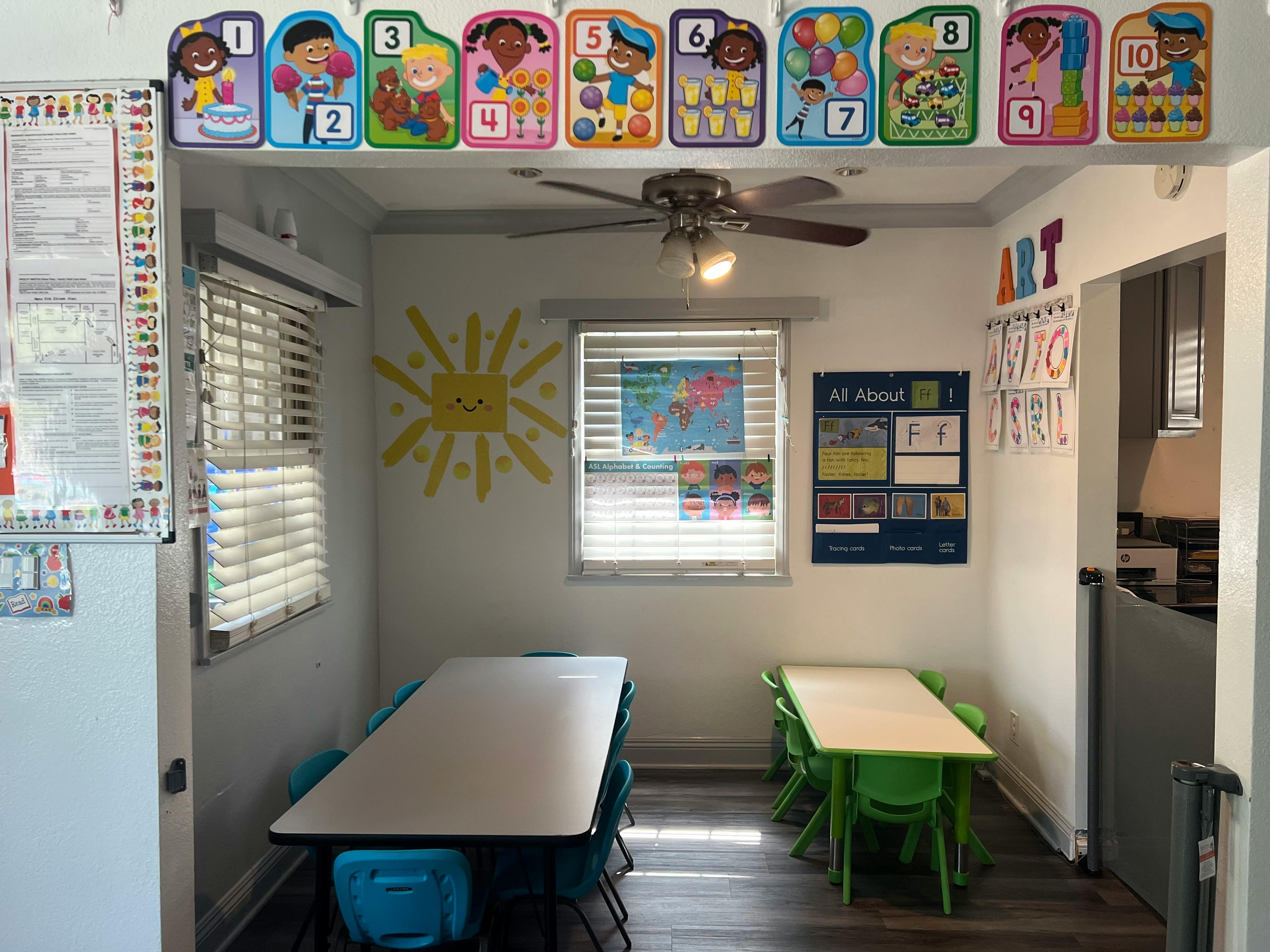 Classroom with tables and chairs, sun decal on wall, and educational posters