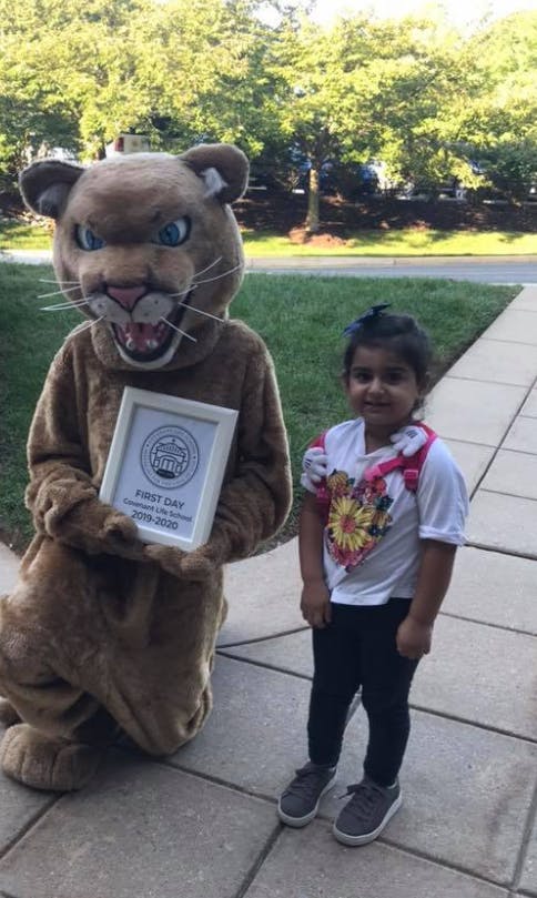 Mascot in a cougar costume holding a framed sign next to a child