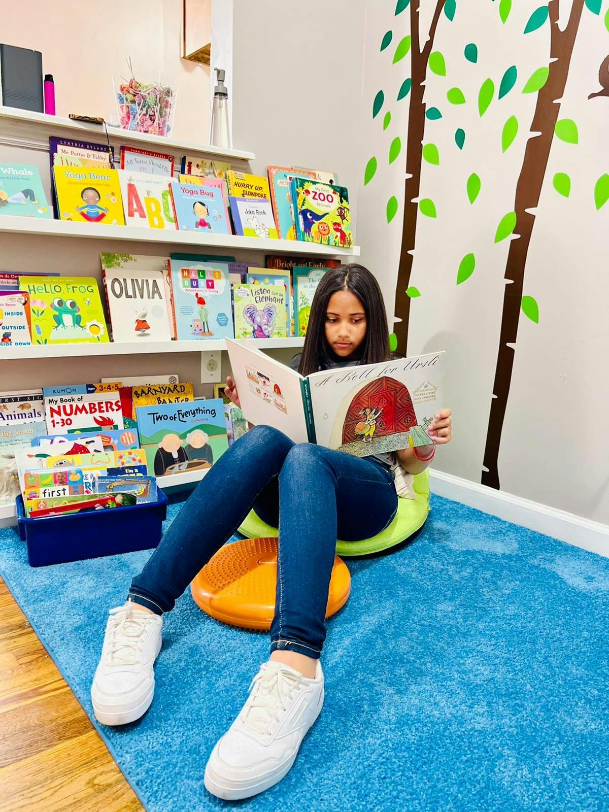 Child sitting on floor reading a book in front of bookshelves