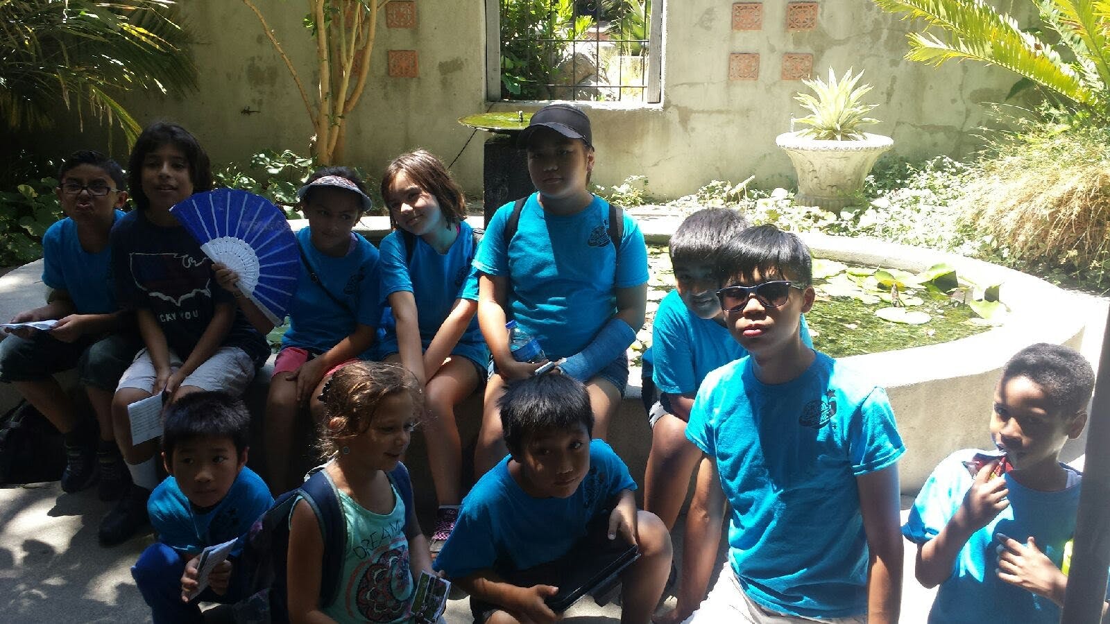 Group of children and teens in blue shirts sitting and standing outdoors