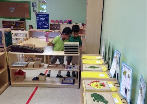 Two children looking at items on a shelf in a classroom