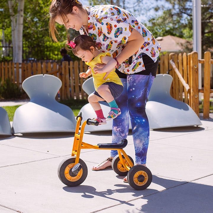 Person helping a child on a small tricycle