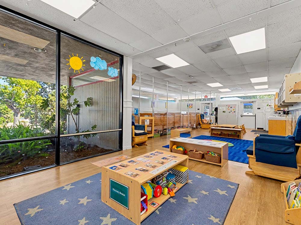 A colorful classroom with natural light, toys, and baby cribs