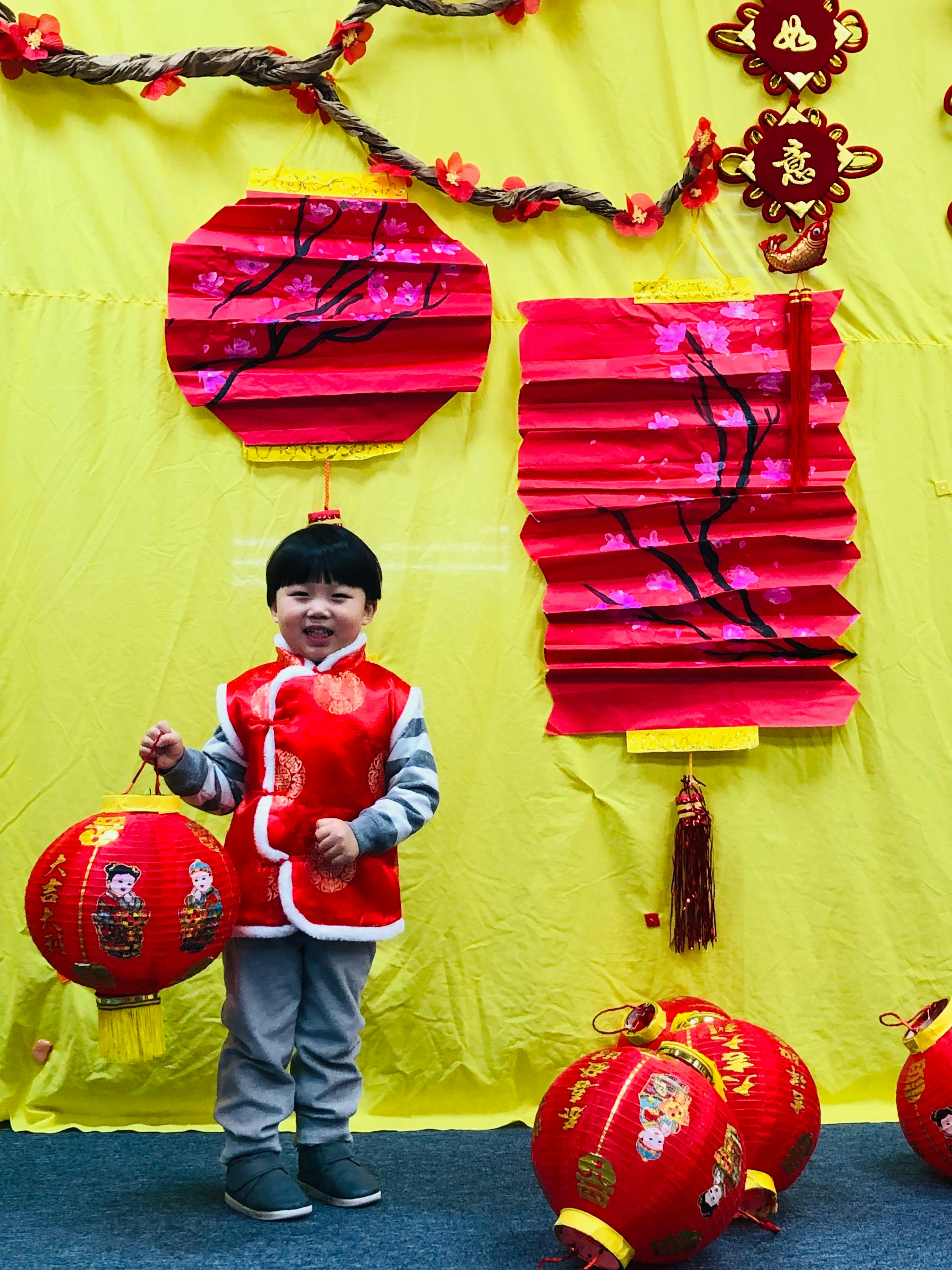 Child in red vest holding a red lantern, with more lanterns in the background