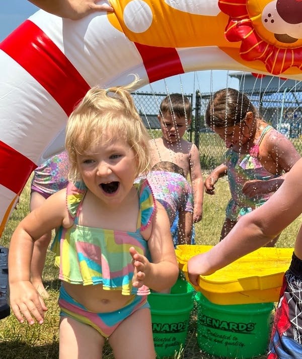 Child in a swimsuit playing under a water sprinkler with other children