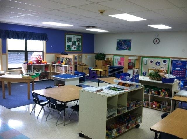 Classroom with small tables and chairs, shelves with toys and supplies