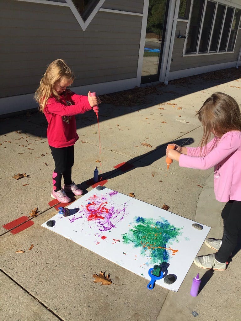 Two children painting on a large white sheet on the ground outdoors
