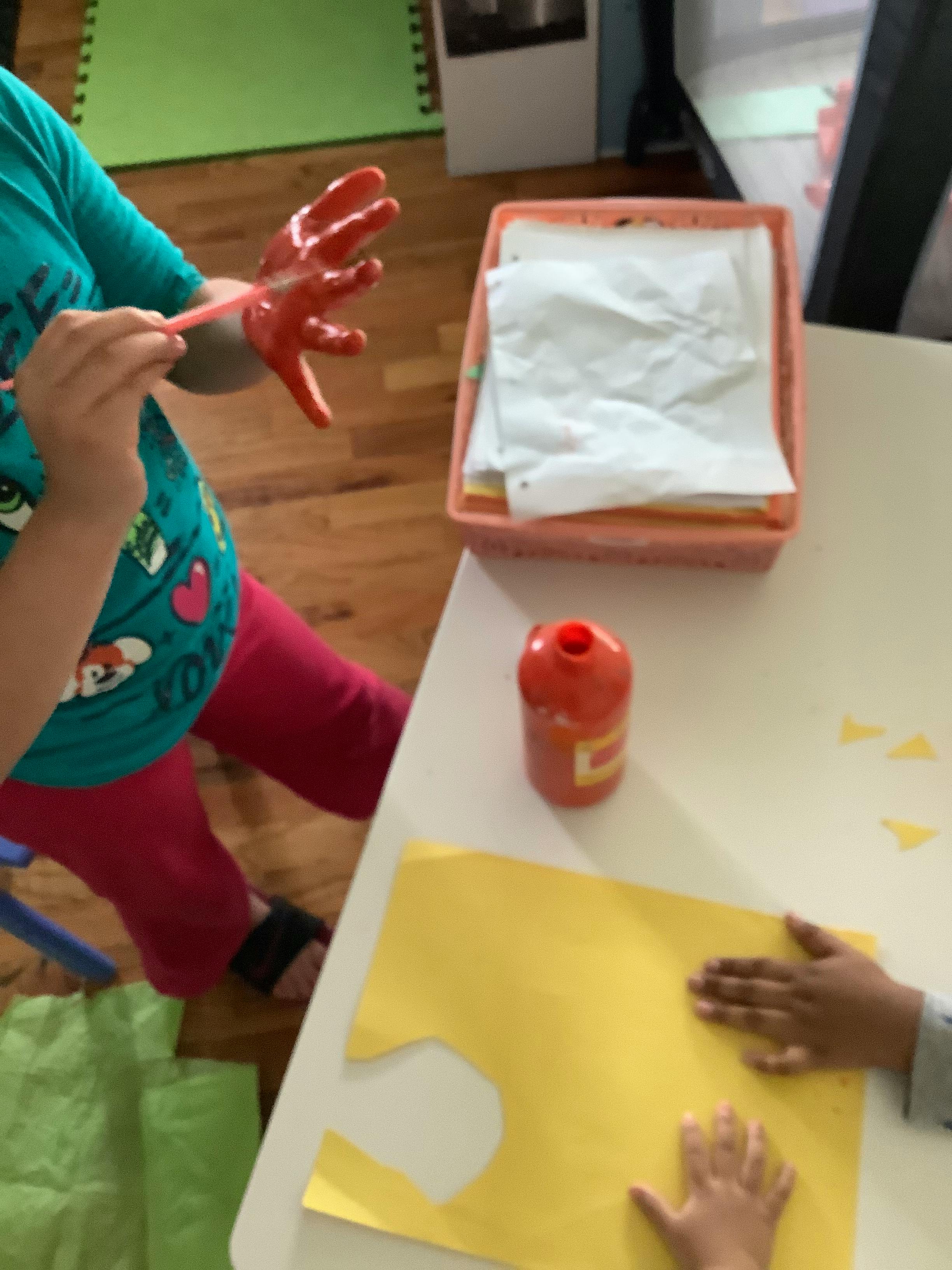 Child painting their hand red with a paintbrush