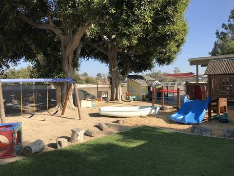 Outdoor playground with swings, slide, and sandbox under large trees