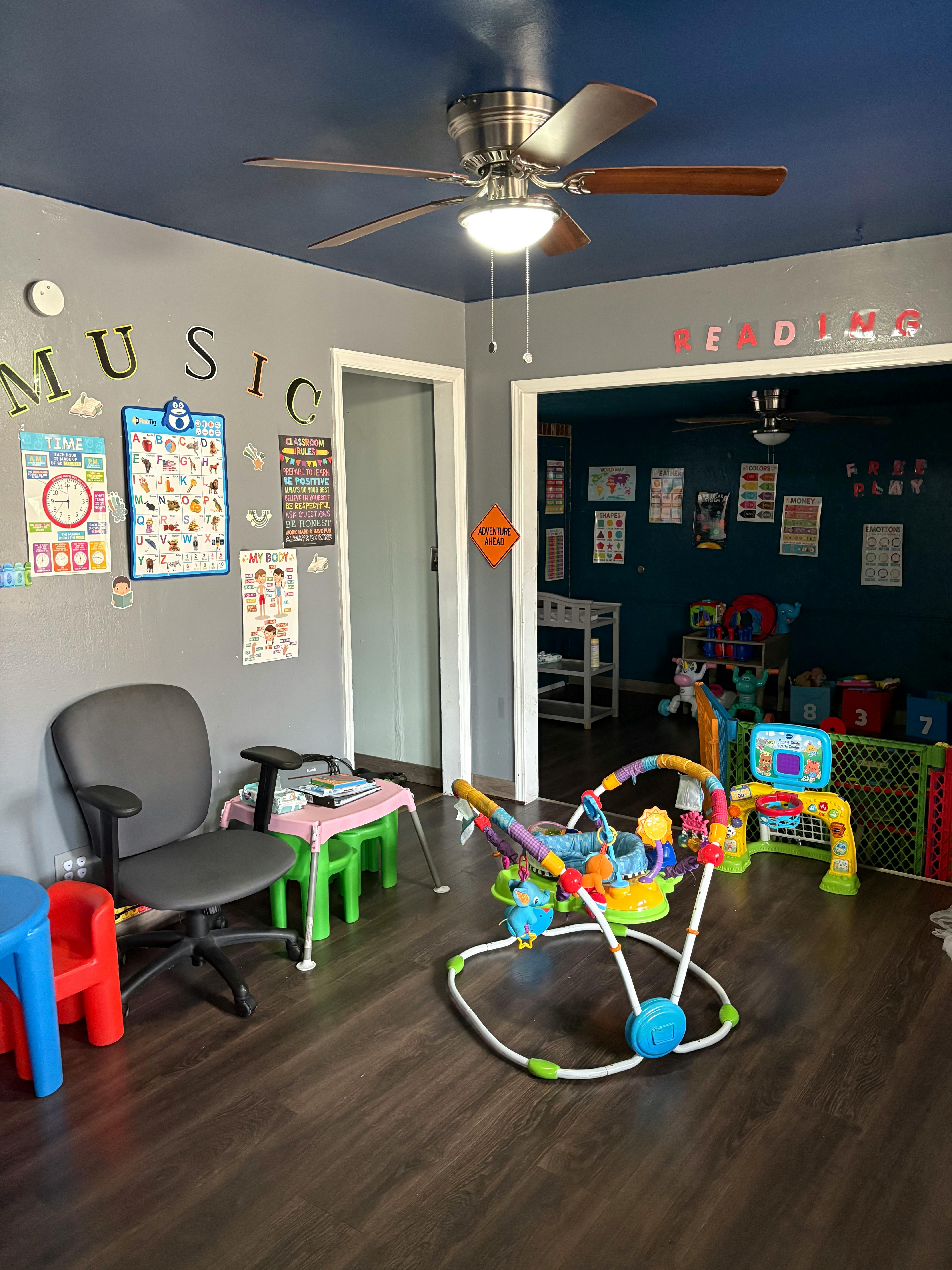 A room with a ceiling fan, a desk chair, and a baby activity center