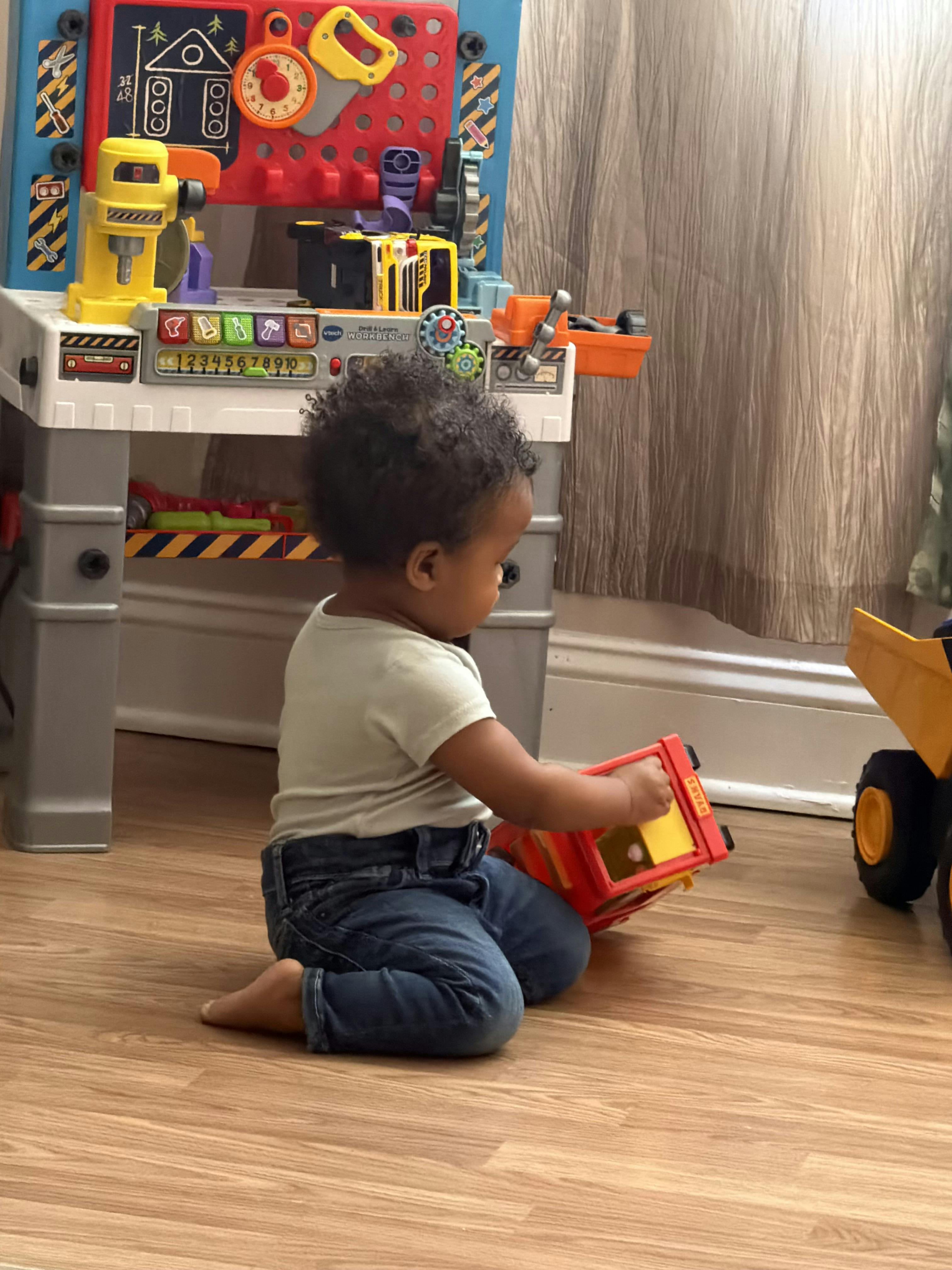 Child playing with a toy truck on the floor in front of a toy workbench