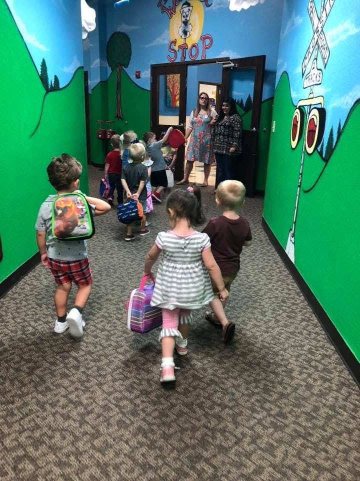 Children walking down a hallway with adults in the background