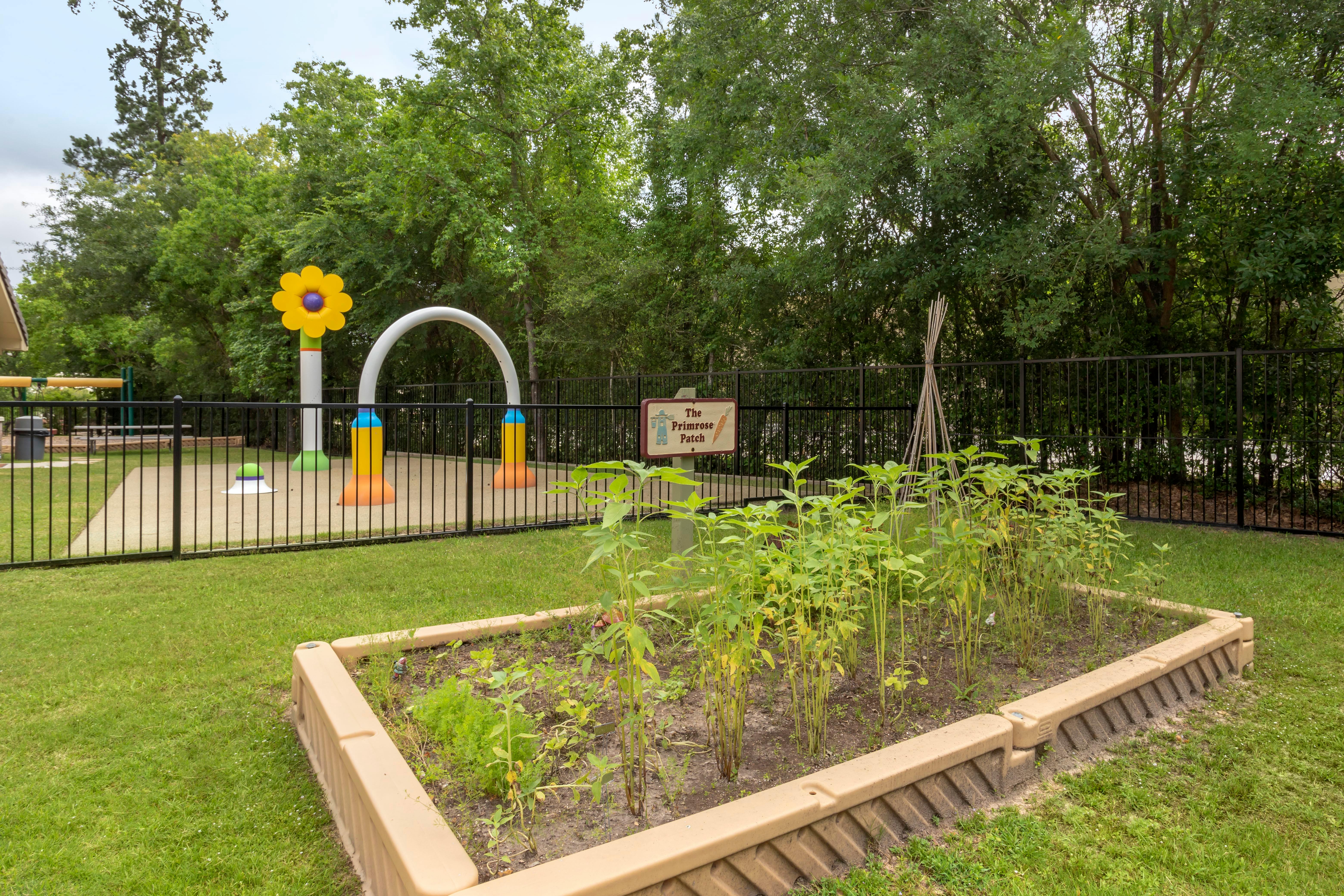 Fenced playground with water features and a raised garden bed labeled "The Primrose Patch"