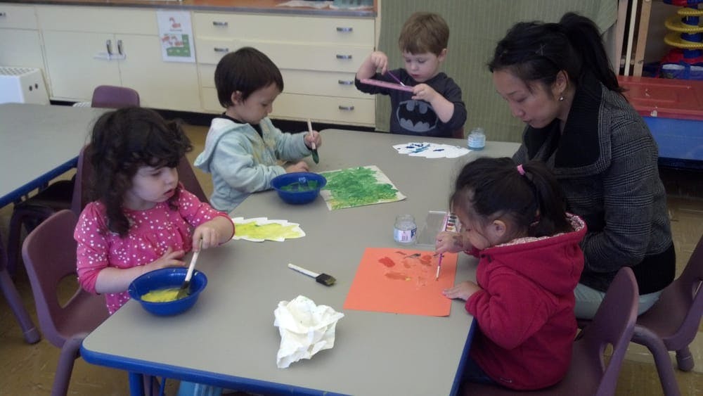 Adult and three children doing an art activity at a table in a classroom