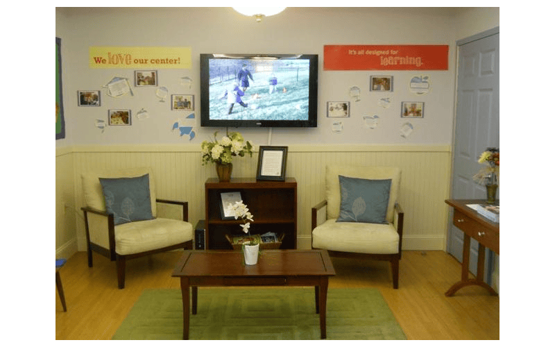 Lounge area with chairs, a coffee table, and a TV showing children playing