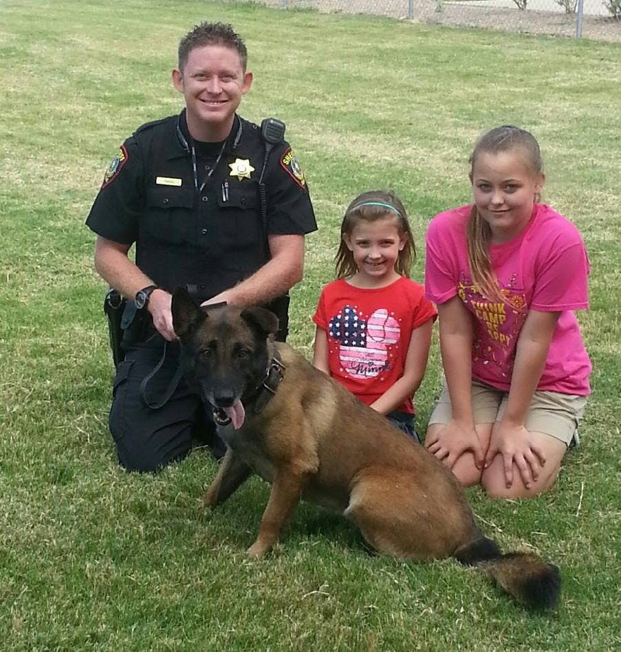 Person in uniform kneeling with two children and a dog on grass