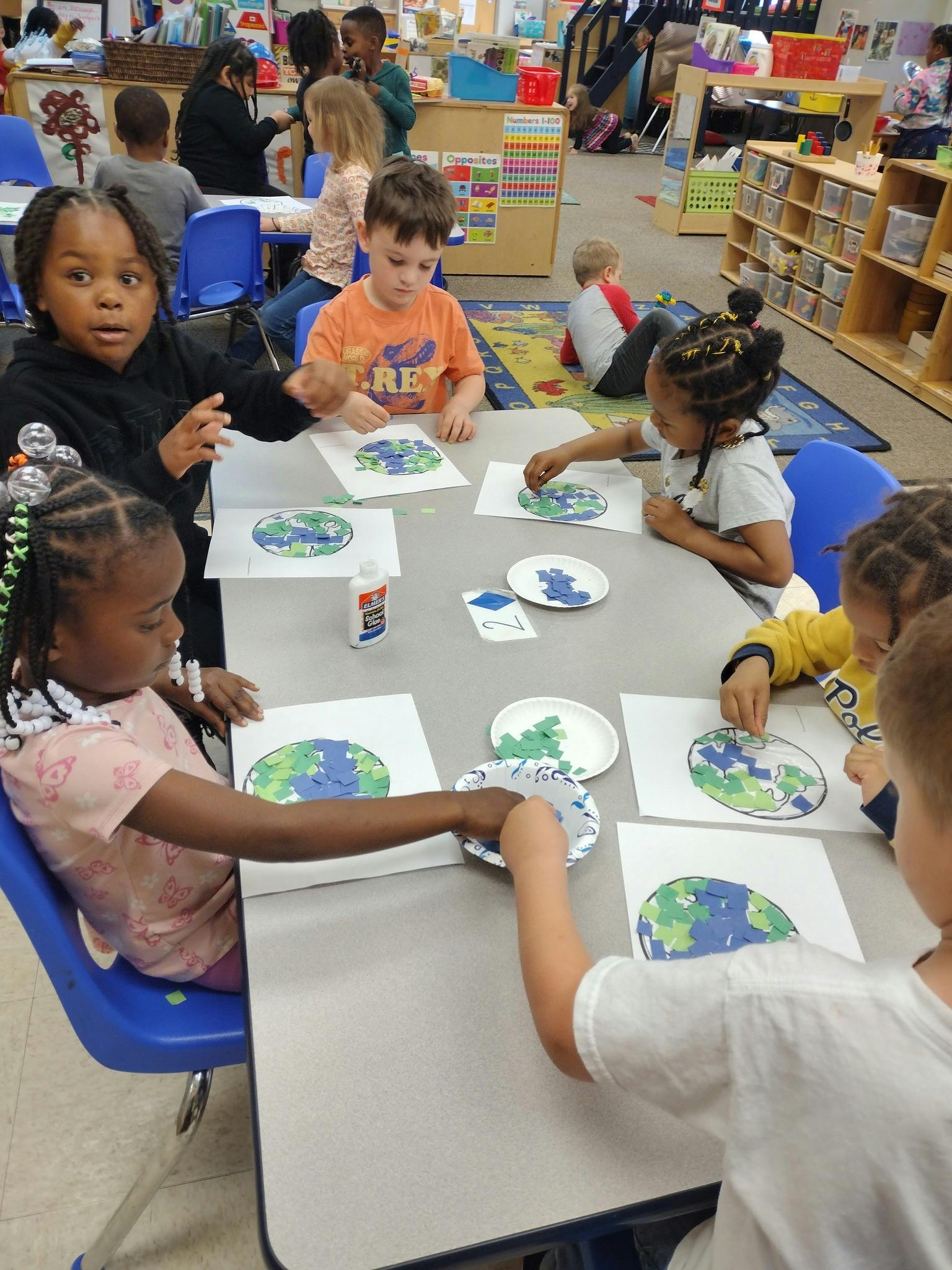 Children at a table doing an art project with paper cutouts of the Earth