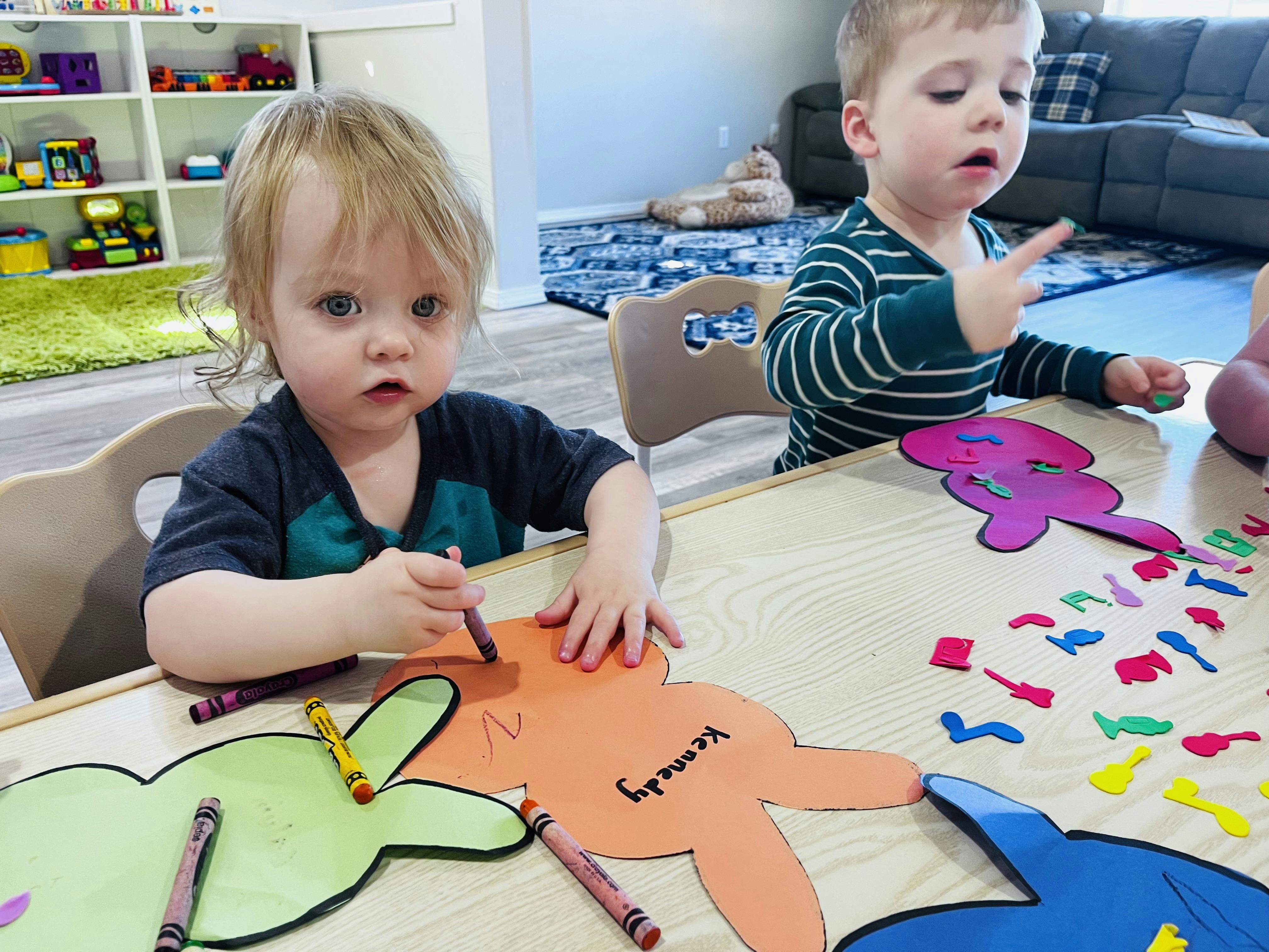 Two children coloring paper cutouts at a table