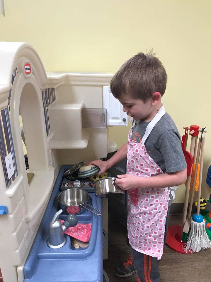 Child in an apron playing with a toy kitchen set