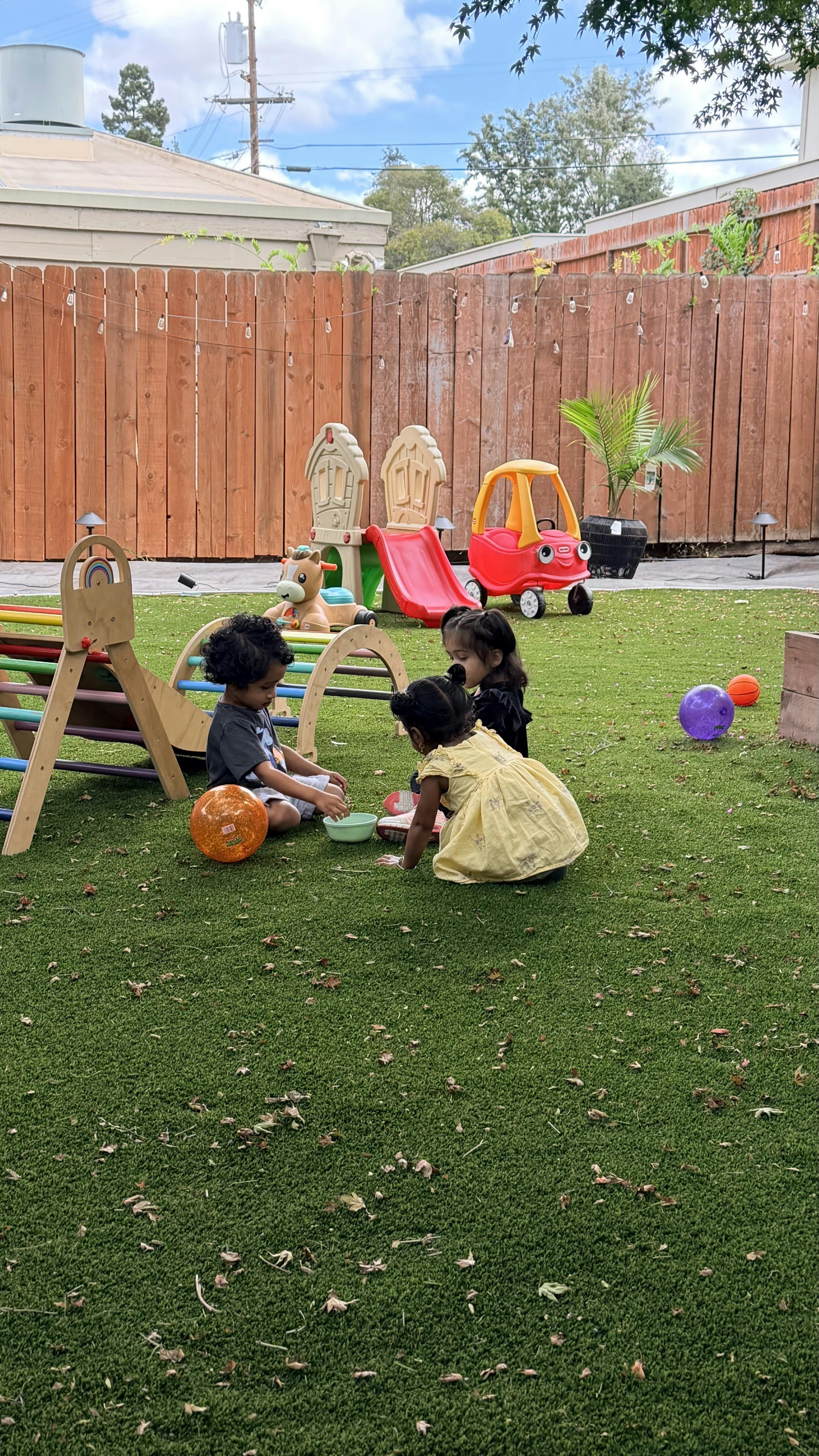 Three children playing together in a backyard on synthetic grass