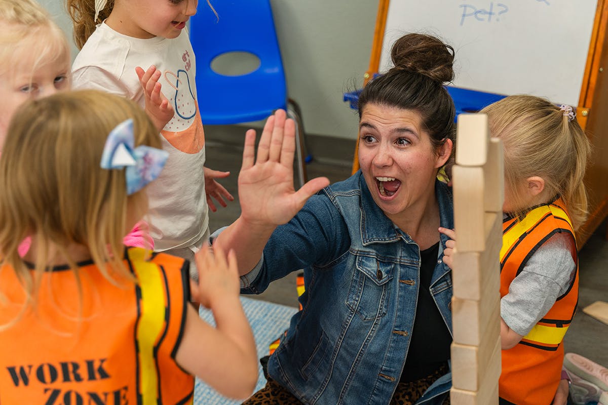 Adult and child high-fiving, with other children nearby