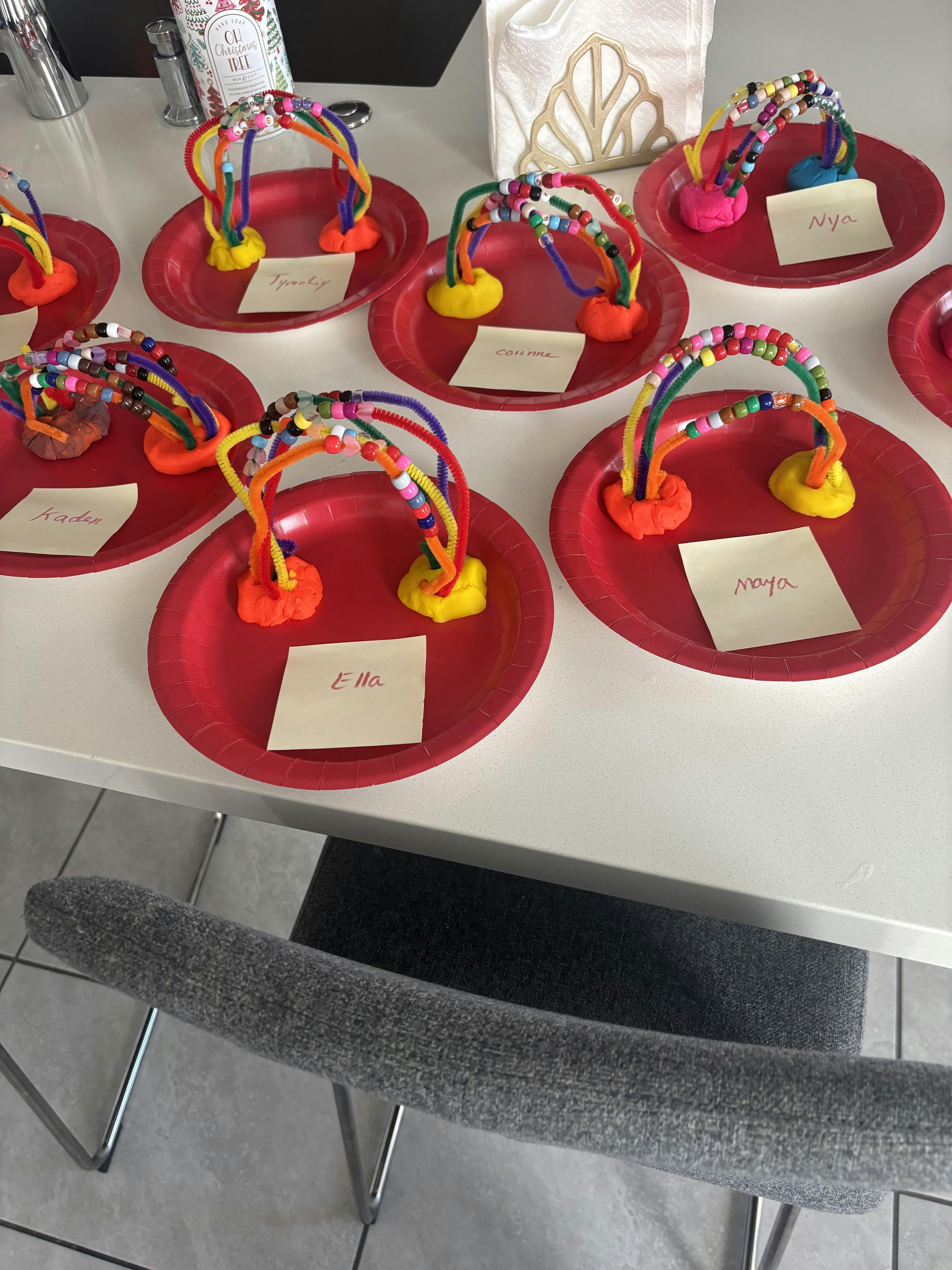 Children's crafts of beaded pipe cleaner rainbows with names on red plates