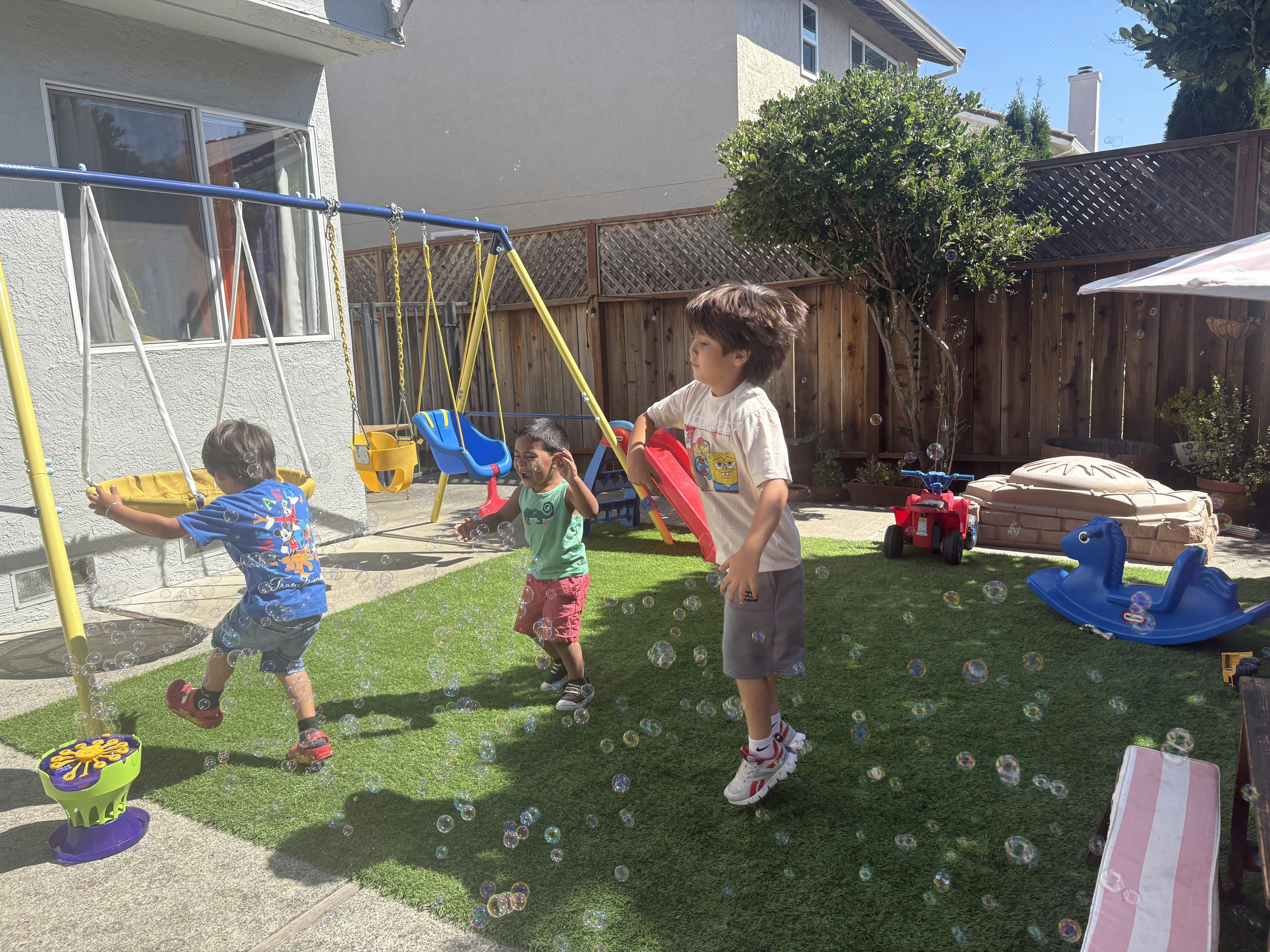 Three children playing with bubbles in a backyard