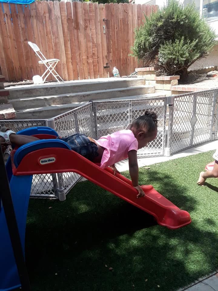 Child sliding down a small red and blue plastic slide headfirst in a backyard