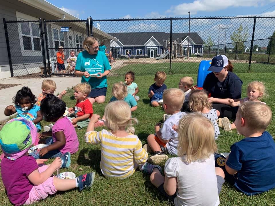 Adults and children sitting in a circle on grass outdoors