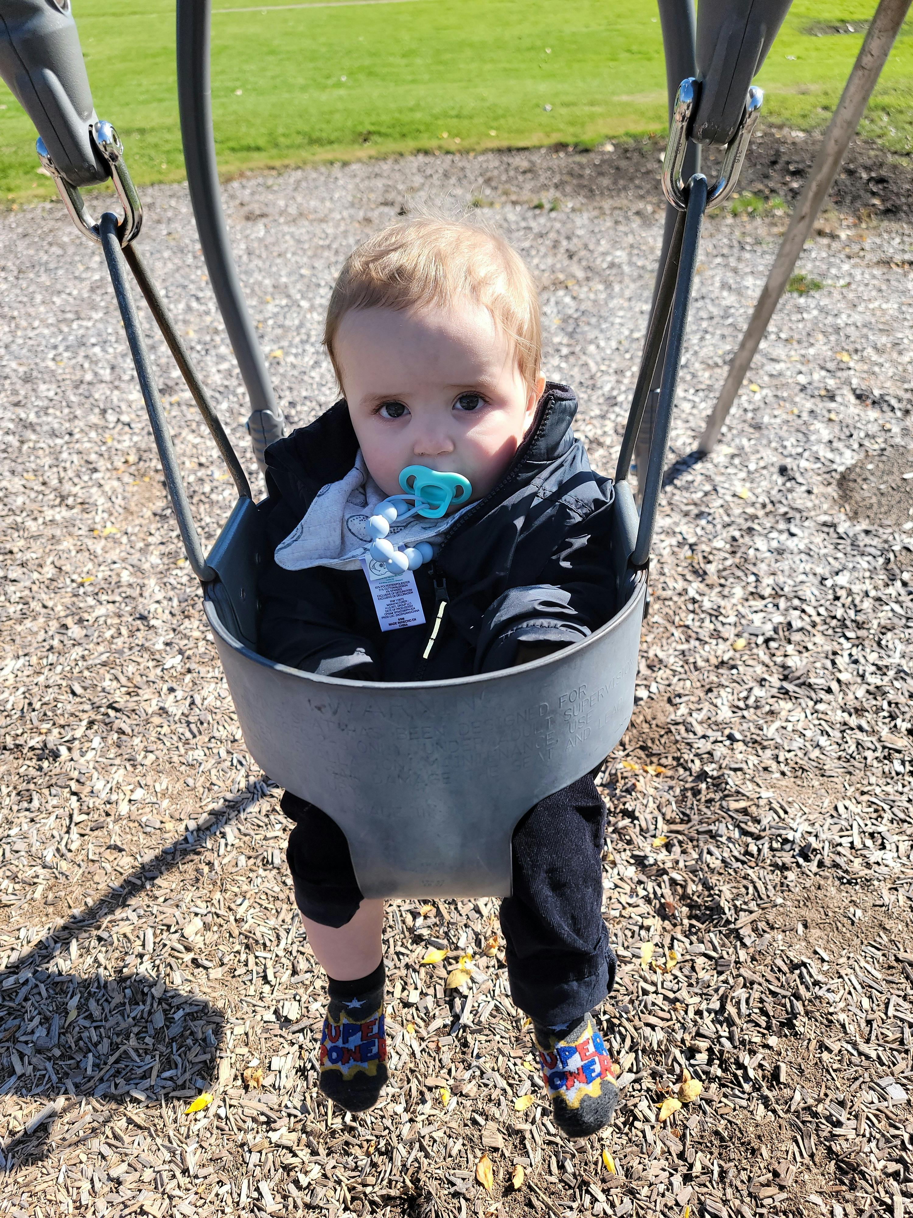 Child with a pacifier sitting in a bucket swing at a playground
