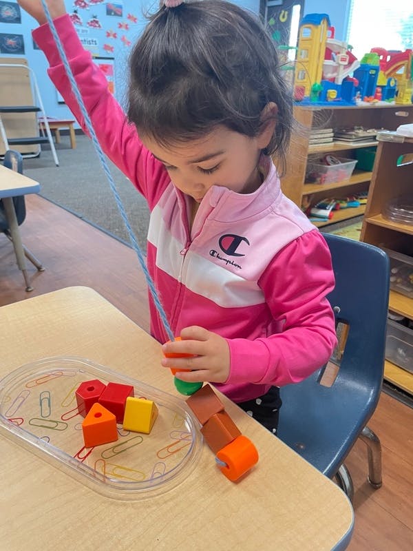Child playing with colorful blocks and string at a table
