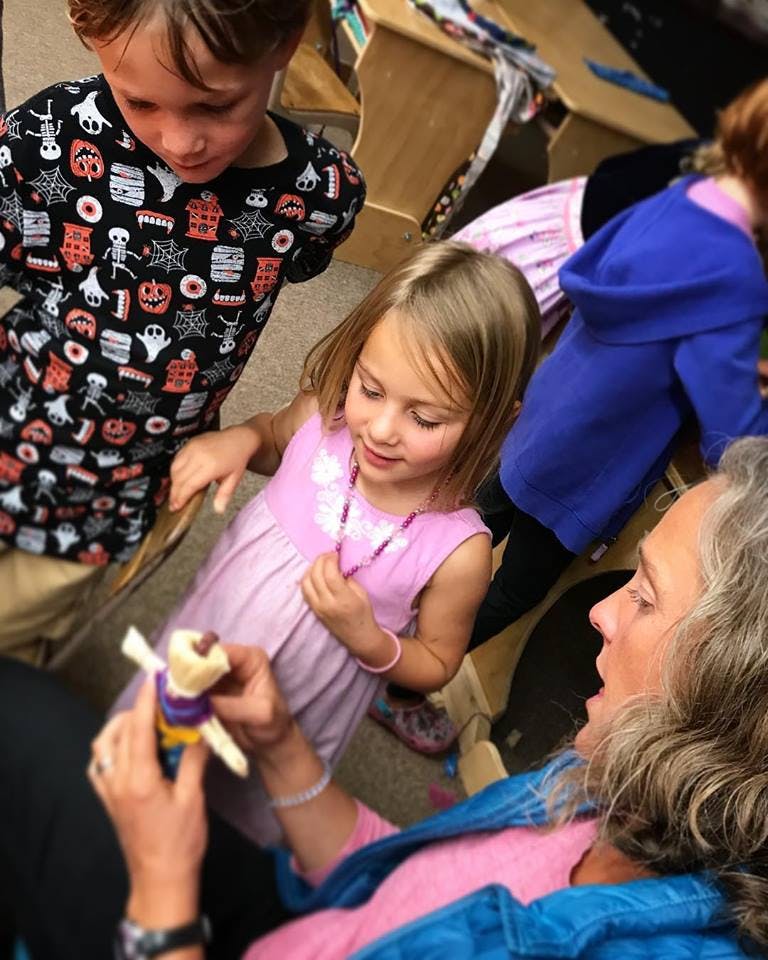 Adult showing a small doll to a child and a teen