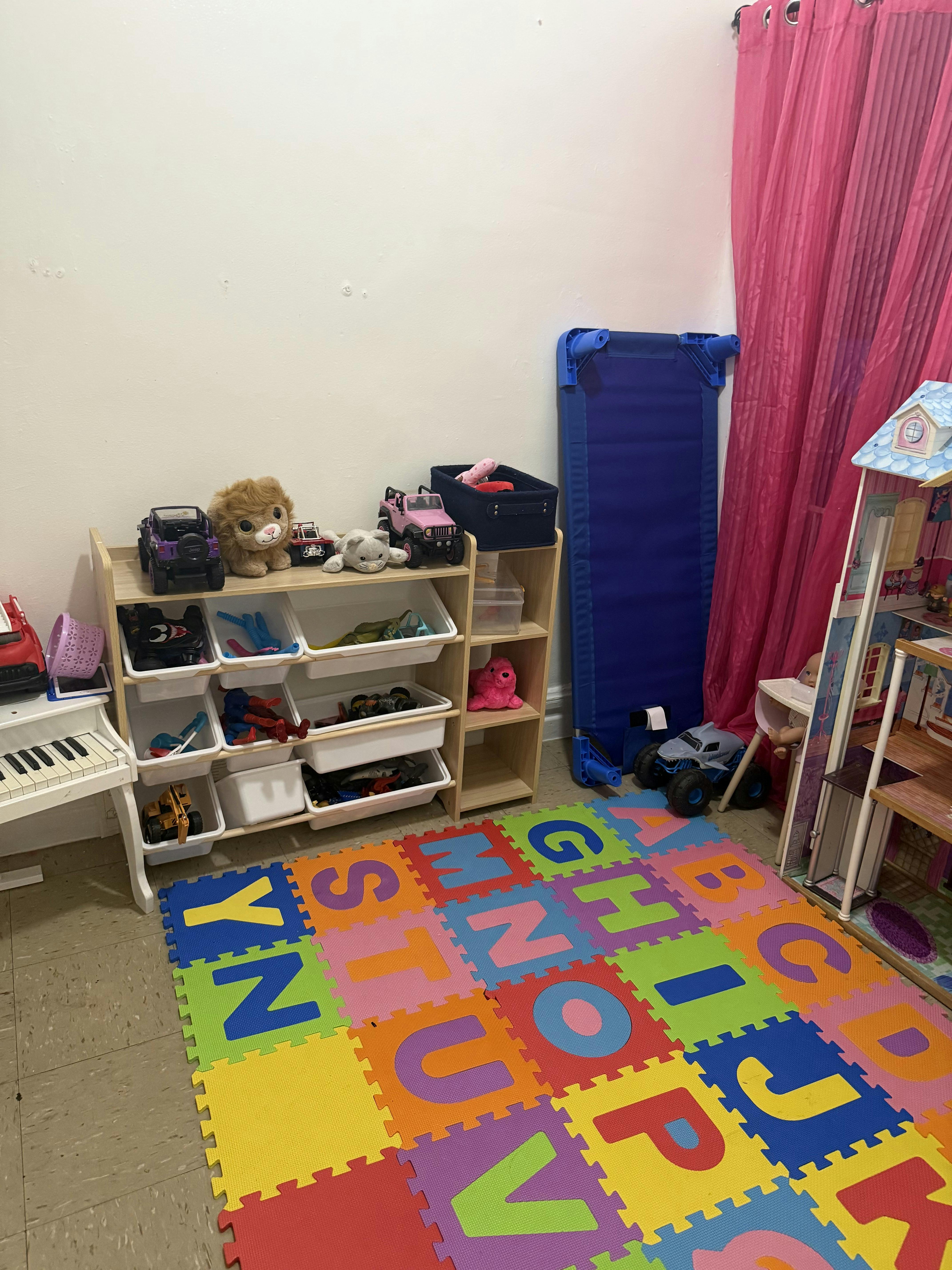 Playroom with alphabet mat, toy shelf, crib, and pink curtain