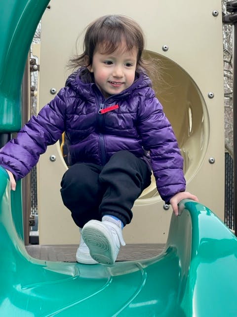 Child in a purple jacket on a green slide