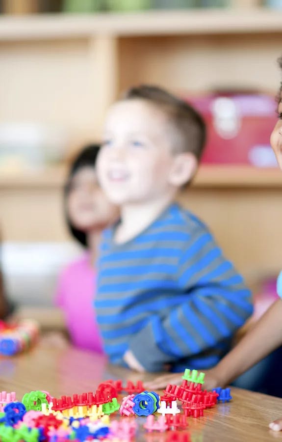 Child in blue striped shirt looking at colorful building toys on a table