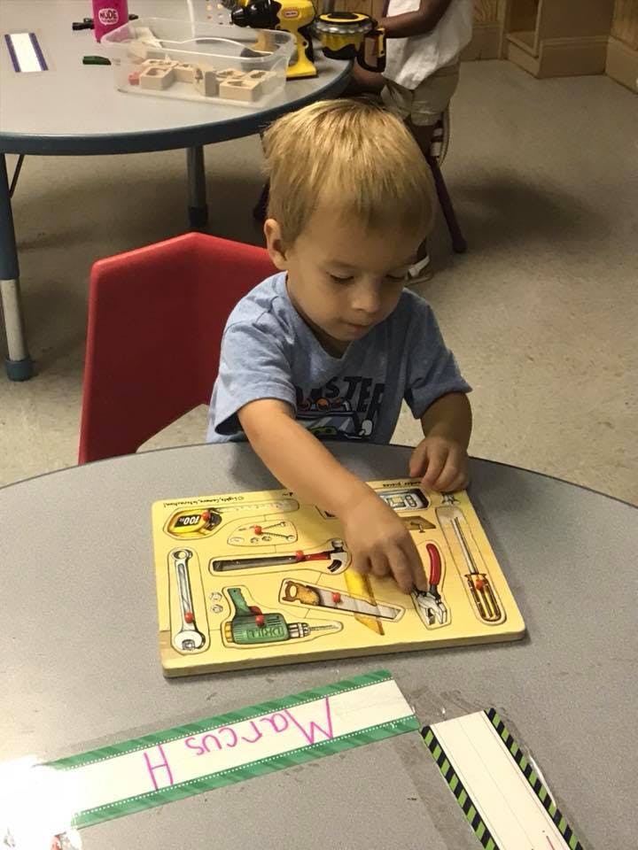 Child playing with a tool-themed puzzle at a table