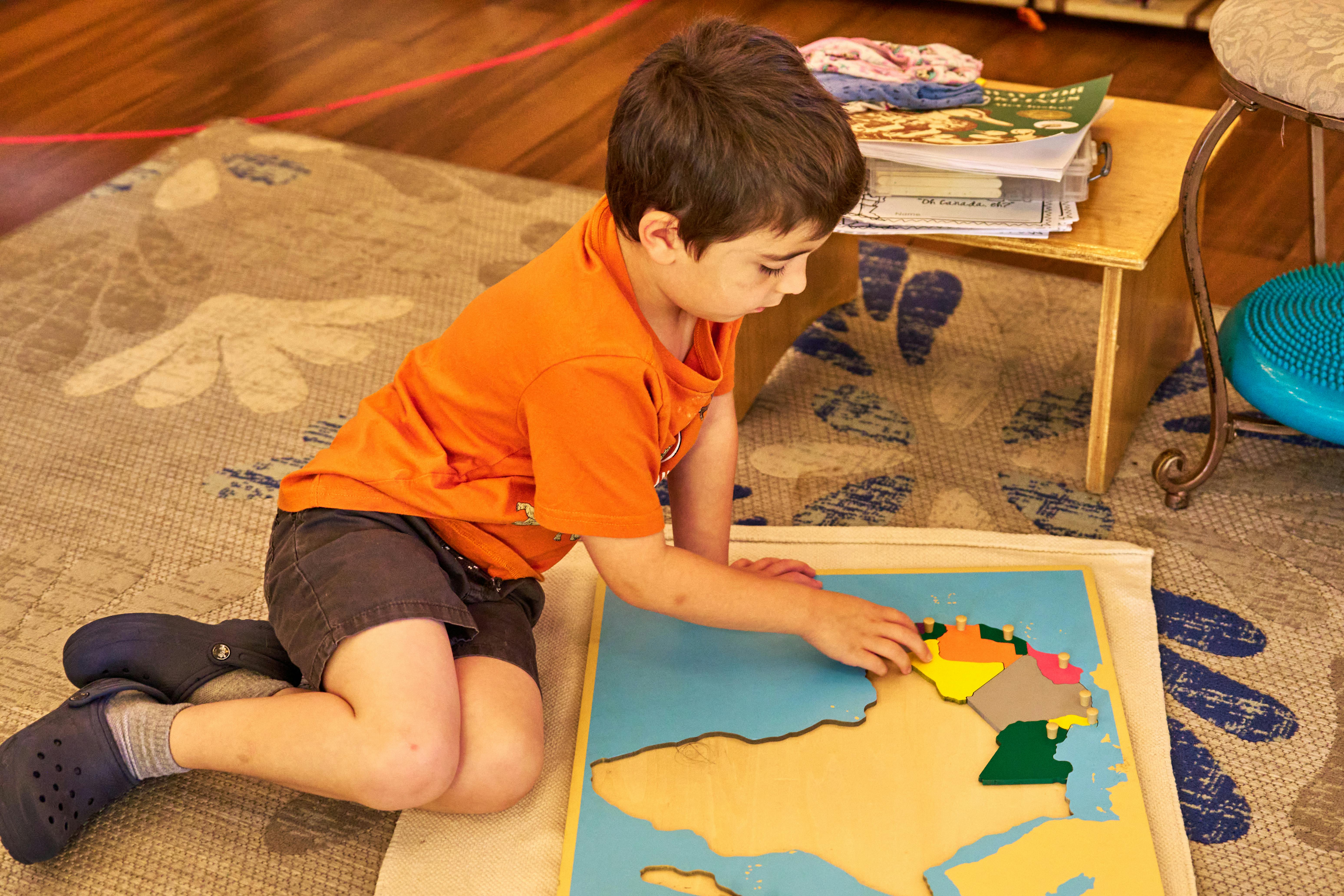 Child kneeling on floor, placing a puzzle piece into a map puzzle