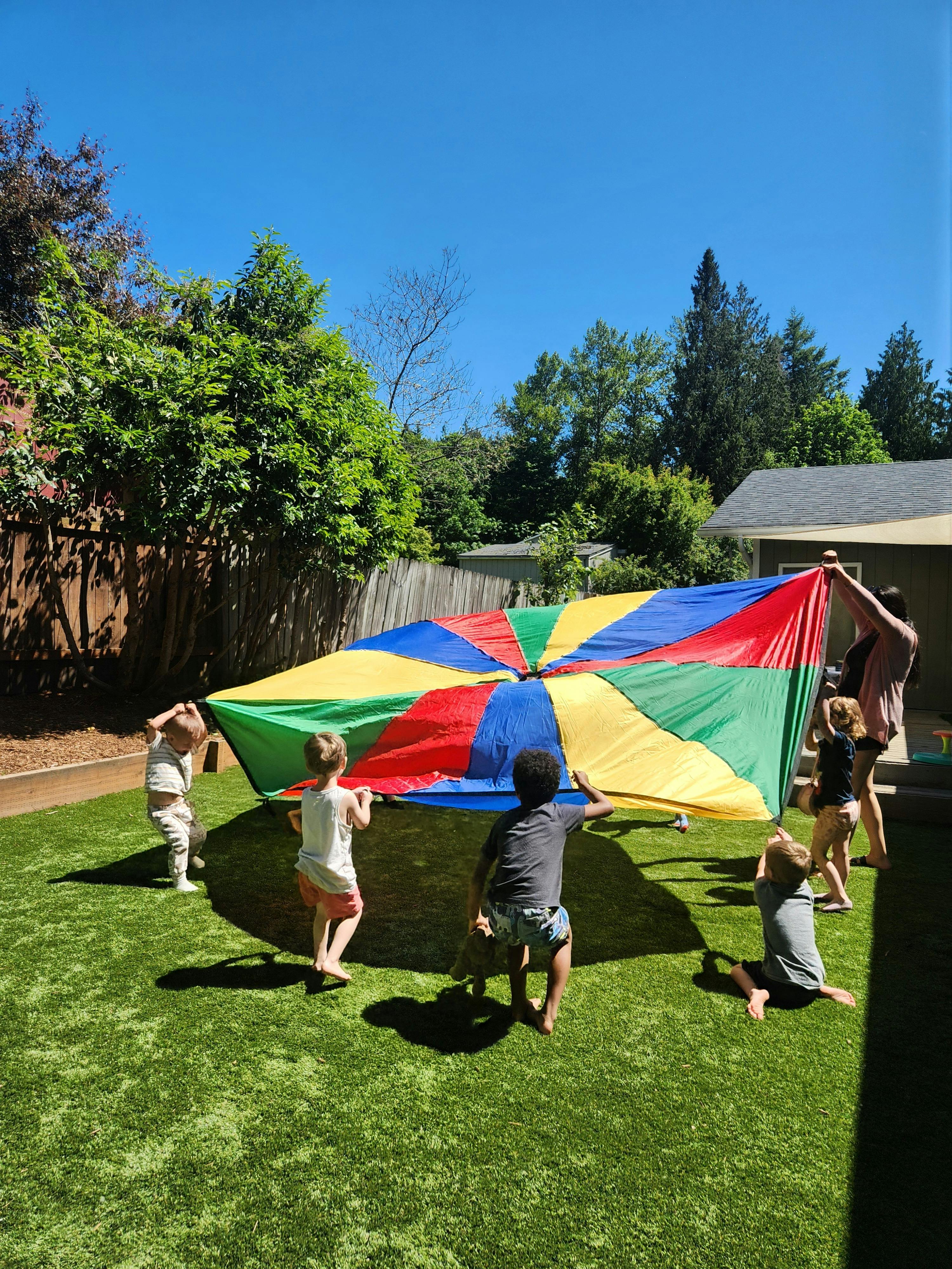 Children playing with a colorful parachute on a grassy lawn